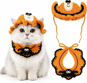 a gray cat wearing a black knitted spider-print bandana around its neck and a small white ghost-shaped knit hat